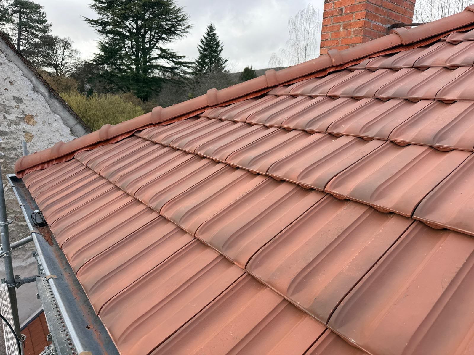 Rangées de tuiles neuves posées autour de la souche de cheminée pendant la réfection de toiture